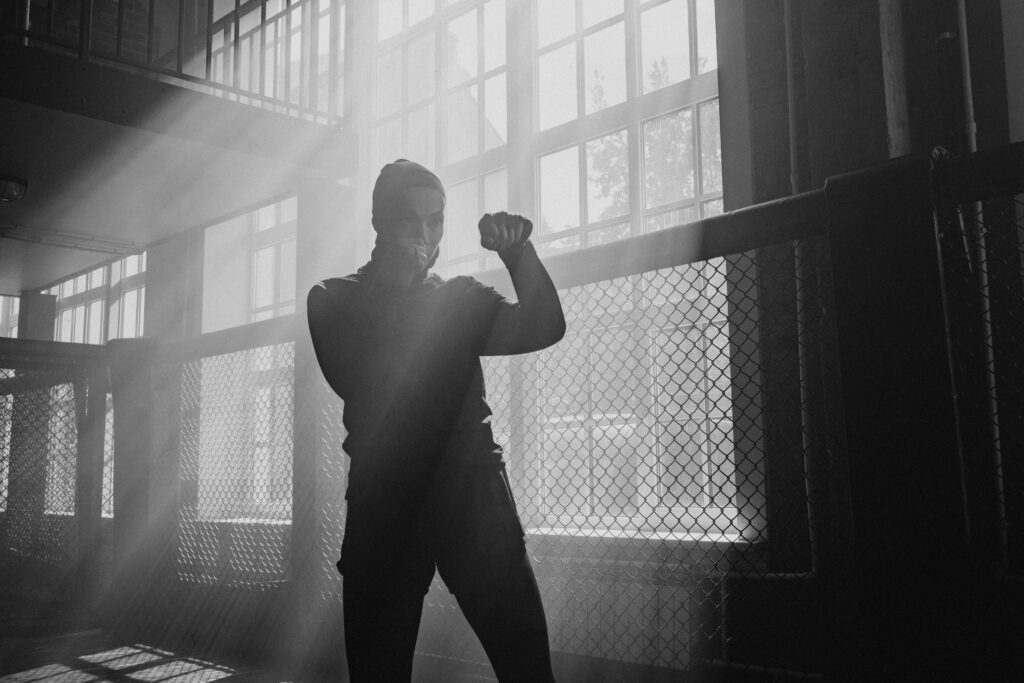 A monochrome image of a boxer training in a sunlit gym, highlighting determination.