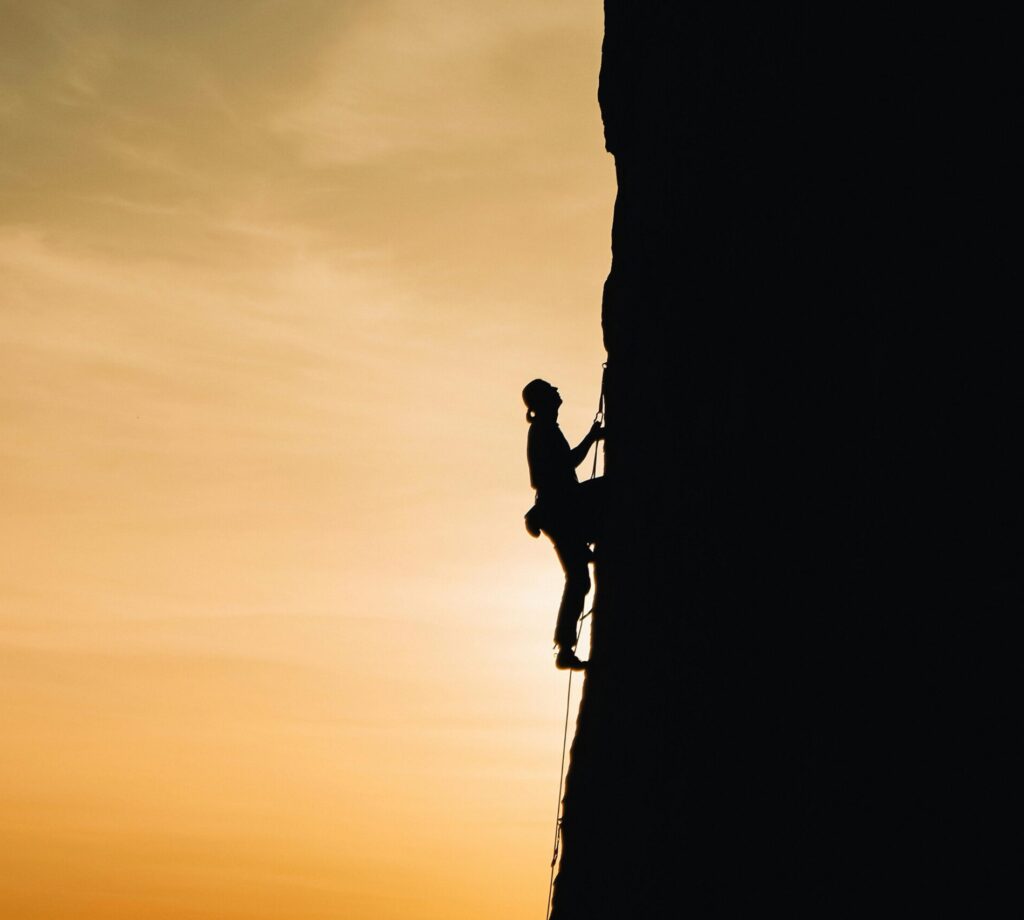 A silhouette of a rock climber scaling a steep cliff during sunset in Russia, showcasing determination and adventure.
