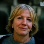 A candid portrait of a senior woman with short blonde hair, outdoors in natural light.
